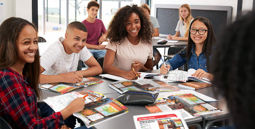 Four students sit together at a classroom table with open books and notebooks