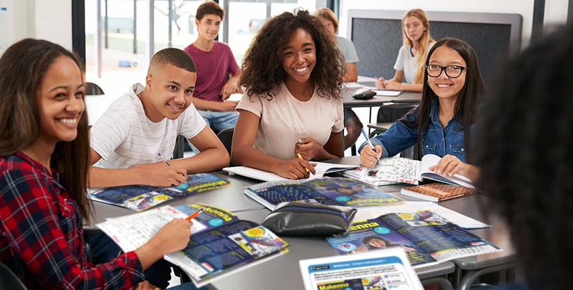 A group of students sit together at a classroom table with open books and notebooks