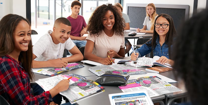A group of students sit together at a classroom table with open books and papers