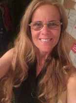 A woman with long wavy hair and glasses smiles at the camera