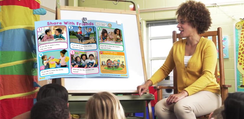 A woman sits in a classroom and presents a Share With Friends poster to a group of young children