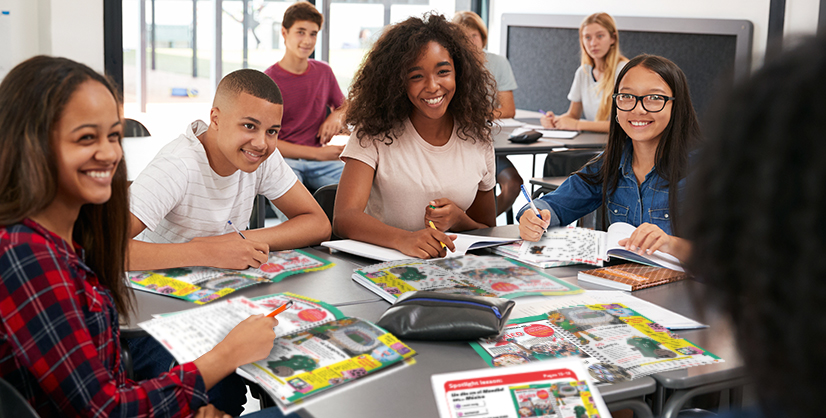 A group of students sit together at a classroom table with open books and notebooks