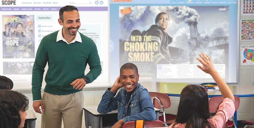 A man stands at the front of a classroom as a student raises her hand
