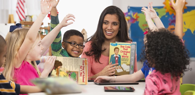 A woman holds up a book titled The Code That Changed the World as children raise their hands