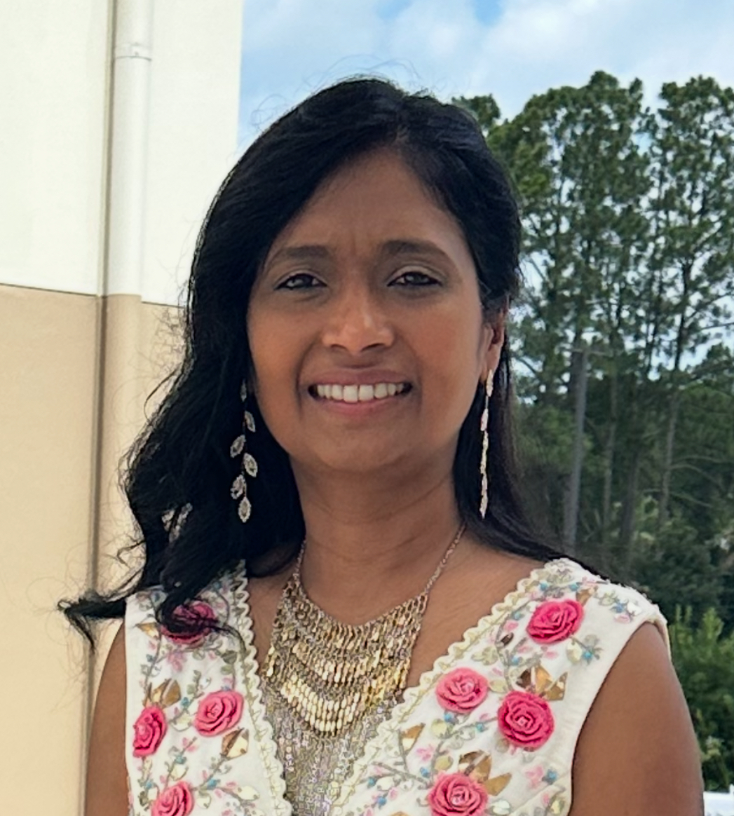 A woman faces the camera outdoors with trees visible in the background