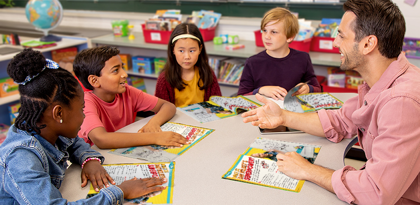 Four students and an adult sit around a classroom table with open magazines or workbooks