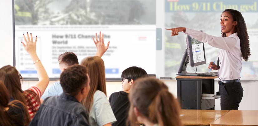 A woman points to a projected screen titled How 9/11 Changed the World as students raise their hands