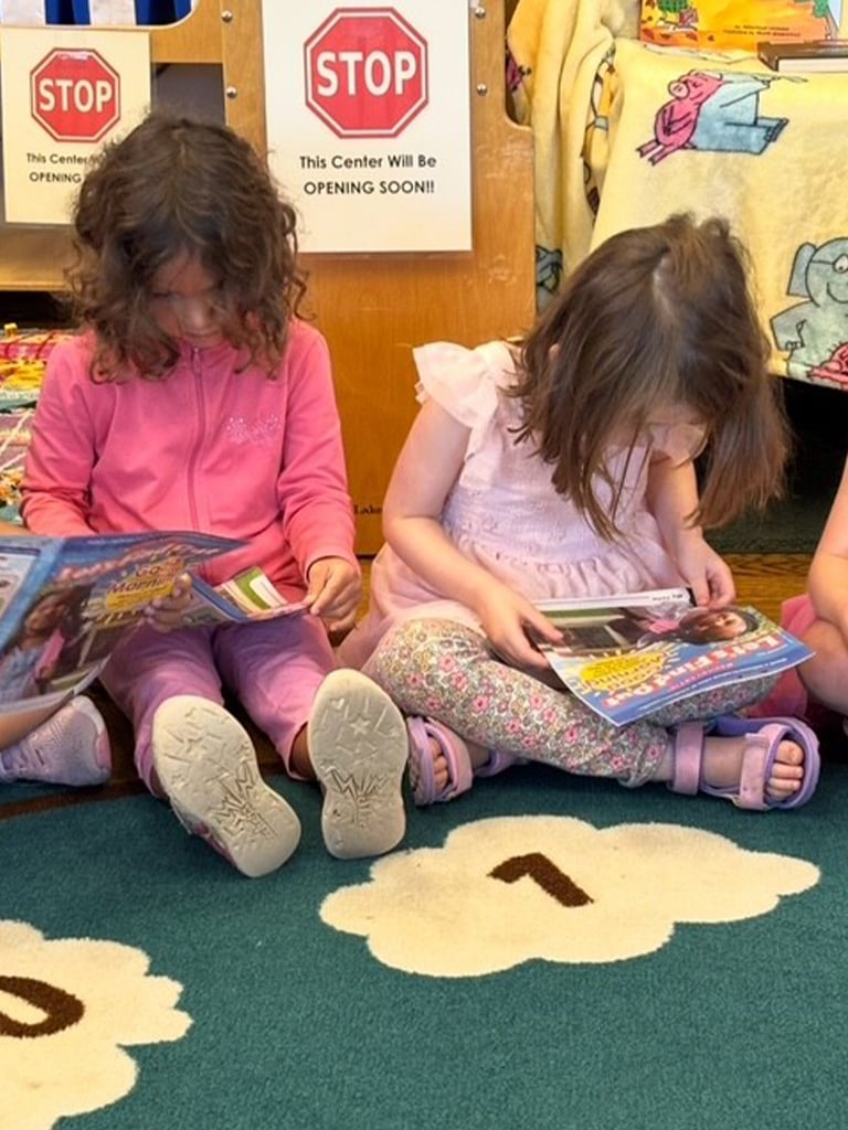 Two girls sit on a classroom floor and read magazines together
